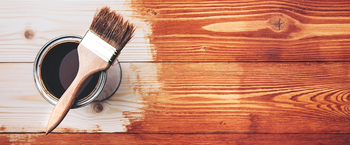 A can of wood floor paints with red stain and a brush