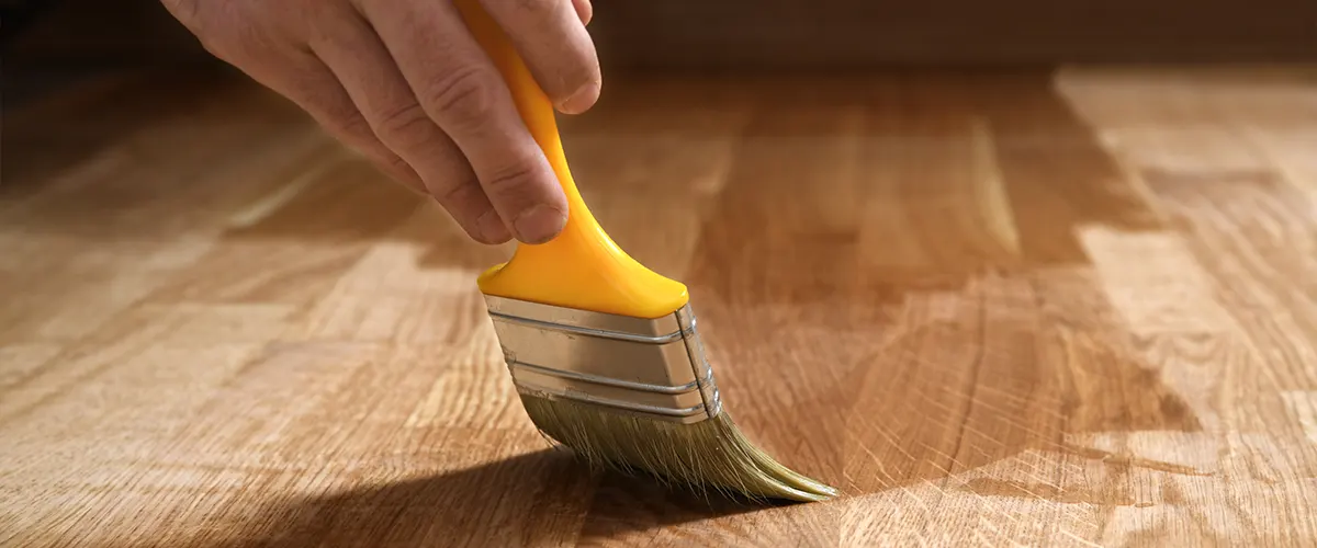 Shellac being applied on a wood surface with a yellow brush