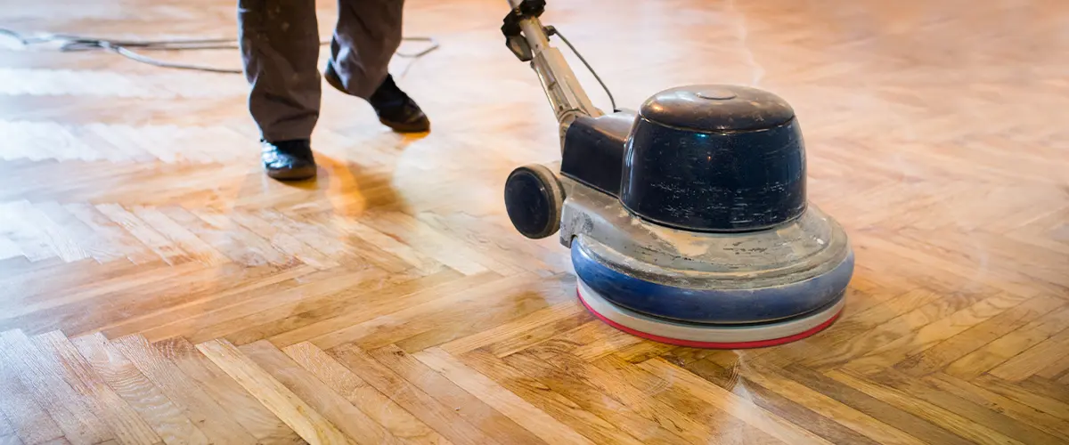 A contractor using a tool to refinish a wood floor