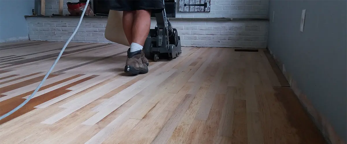 A man refinishing wood floors with a heavy machine