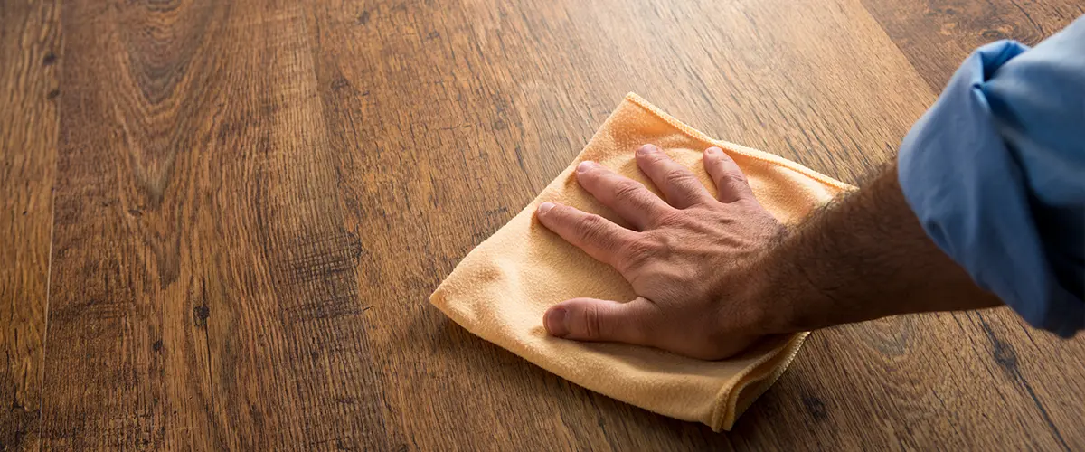 A homeowner cleaning a wood floor with a dry cloth