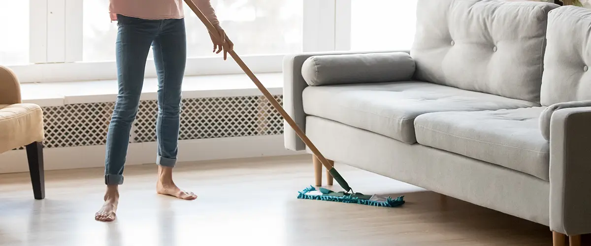A woman mopping underneath a gray couch