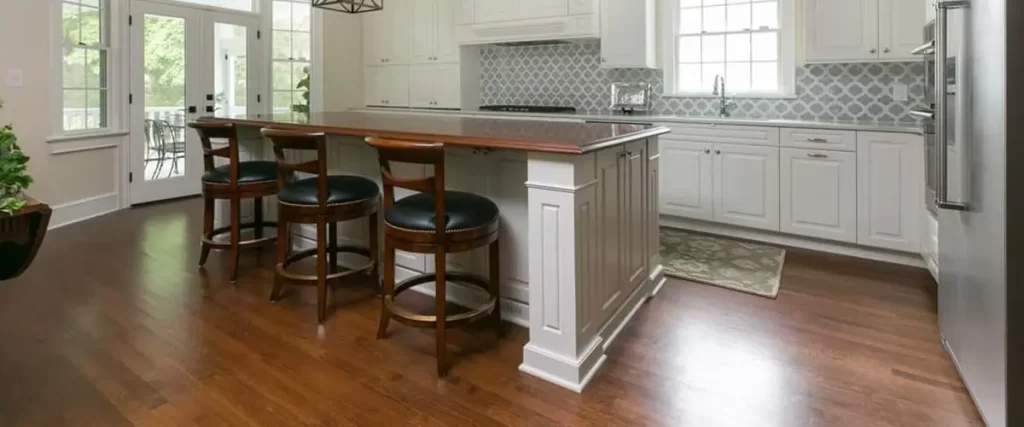 Modern kitchen with hardwood flooring, white cabinets, large island, pendant lighting, and natural light from windows